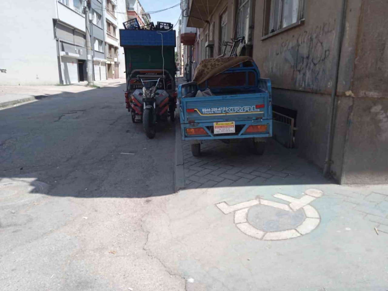 Geri dönüşüm işçilerinin motosikletleri kaldırımdaki engelli rampasını kapatıyor